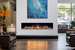 Modern commercial lounge featuring a Flare Front Facing 80” fireplace with a Summit Burner system, set in a clean white wall beneath abstract blue artwork, surrounded by leather seating and large windows with natural light.