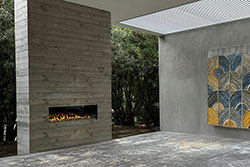 Modern outdoor space featuring a Flare Front Facing 50” Vent Free fireplace built into a vertical concrete wall, surrounded by lush greenery and paired with a geometric art installation under a slatted roof.