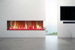 Modern outdoor living area featuring a Flare Right Corner 100” Vent Free frameless fireplace with vivid flames and glass media, built into a smooth white wall overlooking an ocean view beside a mounted TV.